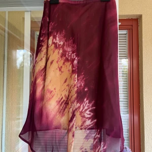 Kjol från Maria Westerlind - Säljer en superfin kjol  från Maria Westerlind i en härlig mix av vinröd och gult. Den har ett unikt batikmönster som verkligen sticker ut. Materialet känns lätt och luftigt, vilket gör den skön att bära. Endast använd ett par gånger. Se även annons för matchande topp. 