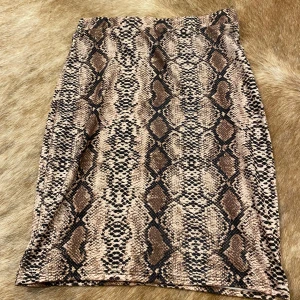 Ormmönstrad kjol - Säljer en supercool ormmönstrad kjol i beige och bruna toner. Kjolen har en tight passform och är perfekt för en utekväll eller fest. Materialet känns mjukt och stretchigt, vilket gör den bekväm att bära hela dagen. Ett måste för garderoben om du gillar djurmönster!