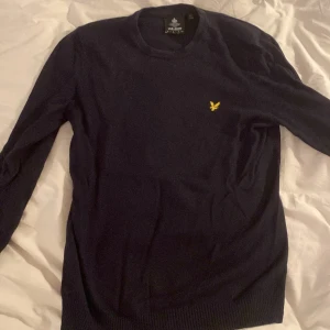 Svart tröja från Lyle & Scott - Säljer en stilren mörkblå tröja från Lyle & Scott i storlek M. Tröjan är långärmad och har en broderad gul logga på bröstet. Perfekt för höst och vinter, och den är gjord i ett mjukt material som känns skönt mot huden. Passar både till vardags och lite finare tillfällen. Passformen är ganska tight, passar alltså som S.