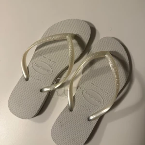 Vita flip-flops från Havaianas - Snygga och bekväma vita flip-flops från Havaianas. Perfekta för sommardagar på stranden eller i stan. De har en klassisk design med en mjuk sula och remmar i syntetmaterial.