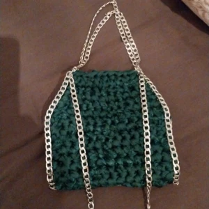 Grön virkad väska med kedjedetaljer - Snygg grön virkad väska med silverfärgade kedjor. Perfekt för att ge din outfit en unik touch. Väskan har en handgjord känsla och är både stilren och praktisk.