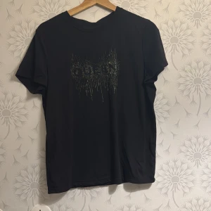 Svart t-shirt med glittrig text - Snygg svart t-shirt med glittrig text på framsidan. Perfekt för en cool och avslappnad stil. Kortärmad och tillverkad i ett mjukt material för extra komfort.