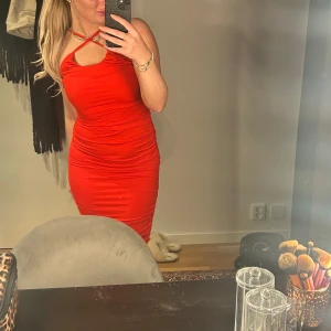 Röd tight klänning - Snygg röd klänning med unik halsdesign och tight passform. Perfekt för en kväll ute eller speciella tillfällen. Klänningen har en smickrande siluett och är axelbandslös med en elegant look.