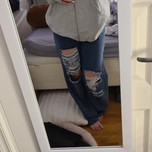 Blå jeans med hål - Säljer ett par blå jeans med hål på framsidan. Stretchiga och mjuka i materialet. Höftmått: 92 cm innerbenslängd:  79 cm. Normal i storleken och inga skavanker.
