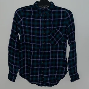 Rutig skjorta i grön/blå färg - Snygg rutig skjorta i blått och grönt med vita linjer. Skjortan har långa ärmar och knappar framtill. Perfekt för en fin vardags look