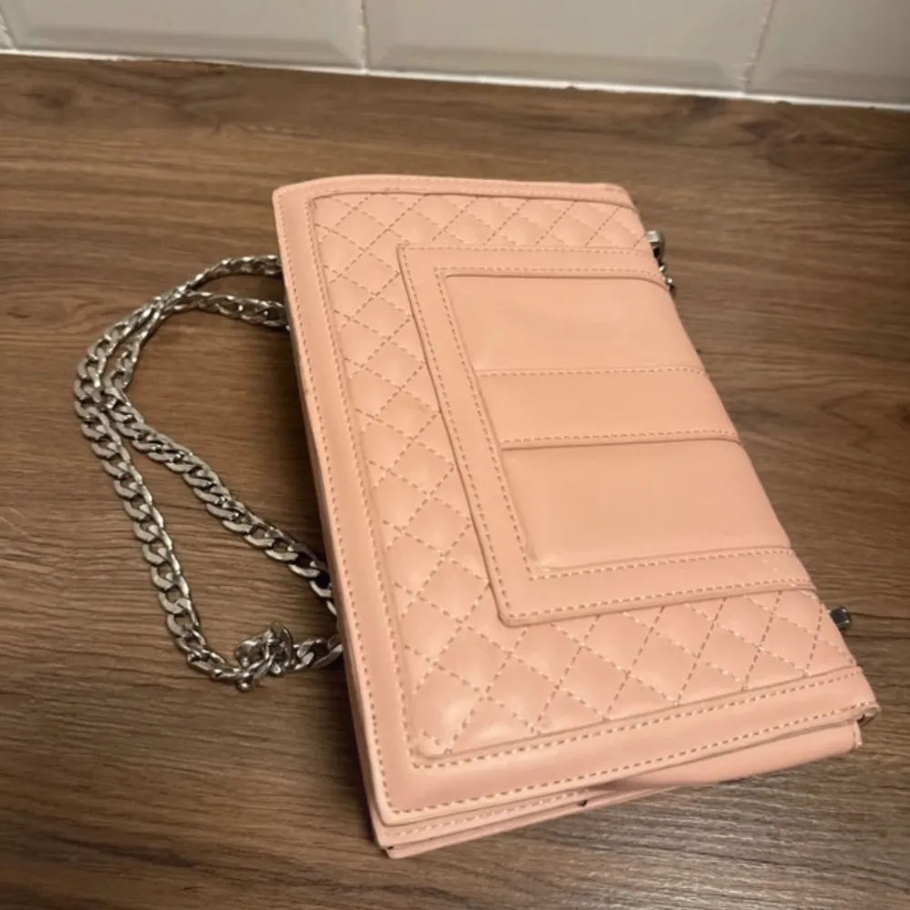 Snygg rosa axelväska med quiltad design och silverfärgad kedja. Väskan har en stilren låsdetalj framtill och är perfekt för att ge din outfit en chic touch.. Laukut & Käsilaukut.