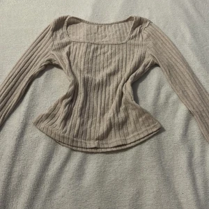 Beige ribbad topp från Shein - Säljer en stilren beige ribbad topp från Shein. Toppen har långa ärmar och en fyrkantig halsringning som ger en modern look. Perfekt för att matcha med olika outfits. Hör av dig vid intresse!