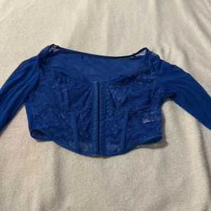 Blå spetskorsett från Shein - Säljer en snygg blå spetskorsett från Shein med långa ärmar i transparent material. Toppen har en elegant design med spetsdetaljer och en åtsittande passform. Perfekt för en stilfull look!