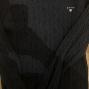 Mörkblå  kabelstickad tröja från GANT - Säljer en stilren mörkblå  kabelstickad tröja från GANT. Tröjan har en klassisk design med rund hals och långa ärmar. Perfekt för kyligare dagar och kan enkelt matchas med olika outfits.