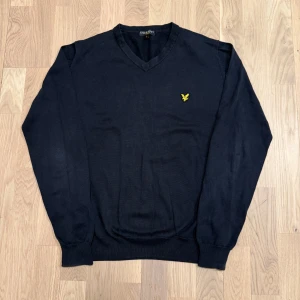Mörkblå tröja från Lyle & Scott - Säljer en stilren svart tröja från Lyle & Scott med v-ringning och deras ikoniska gula logga på bröstet. Tröjan har långa ärmar och ribbade muddar vid ärmslut och nederkant. Perfekt för en klassisk look. Pris kan diskuteras.