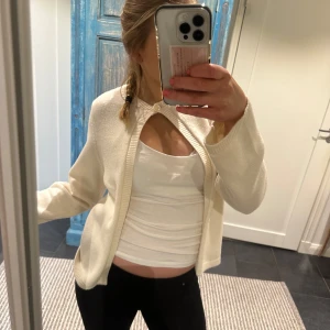 Vit kofta med knäppning - Säljer en stilren vit/begie kofta med en unik knäppning vid halsen. Perfekt för lager-på-lager och ger en elegant touch till din outfit. Passar bra till både vardag och speciella tillfällen. Nästan helt ny knappt använd!!🥰
