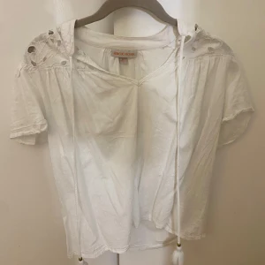 Vit blus från Knox Rose - Säljer en söt vit blus från Knox Rose i storlek XS. Blusen har korta ärmar och fina spetsdetaljer vid axlarna. Den har en v-ringad design med knytband framtill. Köpt i usa kommer inte ihåg var ifrån. 