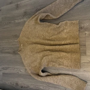 Beige stickad tröja från H&M - Säljer en mysig beige stickad tröja från H&M. Tröjan har en klassisk design med långa ärmar och ribbade kanter vid ärmslut och nederkant. Perfekt för kyligare dagar.