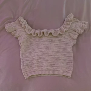 Beige stickad topp från H&M - Säljer en söt beige stickad topp från H&M med volangdetaljer vid halsringningen. Toppen har korta ärmar och en bekväm passform. Perfekt för en stilren look!