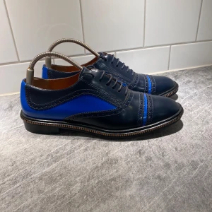 Marc Jacobs skor - Snygga blå och svarta skor från Marc Jacobs med elegant snörning och stilrena detaljer. Skorna är så gått som nya utöver mindre slitningar på undersidan och pytte pytte små märken på hälen 9/10. Nypris är 3570kr och vi säljer för 499. Skorna har en klassisk design med en modern twist, perfekt för att lyfta vilken outfit som helst. Dem har också otroligt fin och högkvalitativ mocka på insidan av hälen (sista bilden). Vid behov av fler bilder eller andra allmäns frågor tveka inte över att kontakta