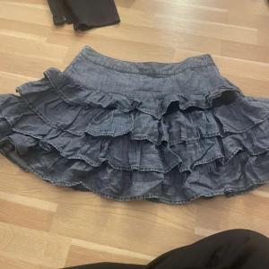 Blå volangkjol från Next - Säljer en blå volangkjol från Next med flera lager av volanger som ger en lekfull look. Perfekt för att lägga till lite extra stil i garderoben. Kjolen har en bekväm passform och är lätt att matcha med olika toppar.