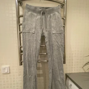 Grå mjukisbyxor från Juicy Couture - Säljer ett par supermysiga grå mjukisbyxor från Juicy Couture i storlek XS. De har en bekväm passform med snörning i midjan och stora fickor fram. Perfekta för en chill dag hemma eller en avslappnad promenad. 🩶