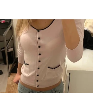 Ljusrosa kofta med svarta detaljer - Säljer en söt ljusrosa kofta med svarta knappar och kantdetaljer. Den har långa ärmar och två små fickor fram. Perfekt för både vår och höst! Lånade bilder från förra säljaren! Funkar i båda S och XS.