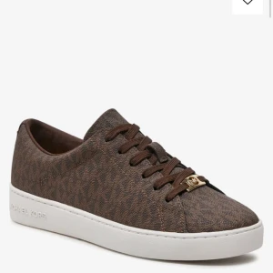 Bruna sneakers från Michael Kors - Snygga bruna sneakers från Michael Kors i mycket bra skick. De har en stilren design med snörning och en vit sula som ger en fräsch kontrast. Perfekta för både vardag och festliga tillfällen!