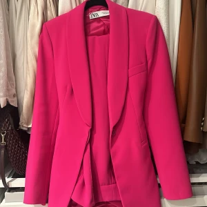 Rosa kavaj och byxor från Zara - Säljer en snygg rosa kostym från Zara i storlek XS. Kavajen har en klassisk design med knappar och byxorna är i en matchande färg. Perfekt för fest eller en chic vardagslook. Kostymen är i mycket bra skick och ger en färgklick till garderoben!