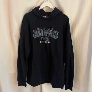 Oversized hoodie med tryck - Säljer en helt oanvänd marinblå hoodie med texten 'athletics IVER' på framsidan. Den är oversized och har en klassisk design med huva och långa ärmar. Supermysig invändigt!! Köpt på eventet ”Hip Hop Weekend” under Malmö Dance Week.