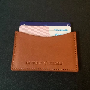 Kortfodral i läder från Sandlund/Hossain - Säljer ett stilrent och praktiskt brunt kortfodral i läder från Sandlund/Hossain. Perfekt för att hålla dina kort organiserade och lättillgängliga. Fodralet har en enkel design med plats för flera kort. Passar perfekt i fickan eller väskan! Pris kan diskuteras.