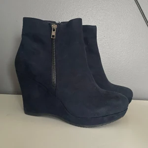 Svarta kilklackade boots med dragkedja - Snygga svarta boots i mocka med kilklack och dragkedja på sidan. Perfekta för höst och vinter, dessa boots ger både stil och komfort. De har en elegant design som passar både till vardags och fest.