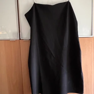 Svart klänning från H&M - Snygg svart axelbandslös klänning från H&M i storlek L. Perfekt för festliga tillfällen med stilrena detaljer och en elegant passform. Klänningen har en glittrig kedja som ger en extra touch av glamour. Passar utmärkt till nyår eller andra speciella tillfällen.
