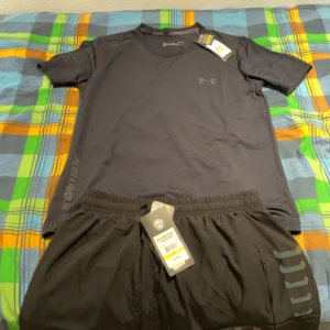Svart träningsset från Under Armour - Säljer ett nytt svart träningsset från Under Armour. T-shirten är kortärmad och har en normal passform, perfekt för träning.  Setet är i storlek M och har märkets logga diskret på bröstet och byxorna. Helt ny!