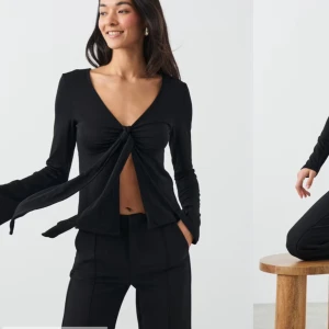 Svart knytblus - Snygg svart blus med knytning framtill och v-ringad design. Perfekt för både vardag och fest. Den har långa ärmar och en elegant passform som framhäver figuren. Ett måste i garderoben för en stilren look! Jag säljer denna för den aldrig har kommit till användning💗