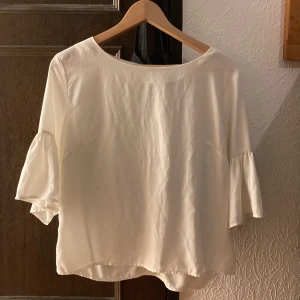 Vit blus med trekvartsärm - Säljer en stilren vit blus med trekvartsärm. Blusen har en lös passform och är perfekt för både vardag och fest. Den är tillverkad i ett mjukt och bekvämt material som faller fint. Passar bra till både jeans och kjol!