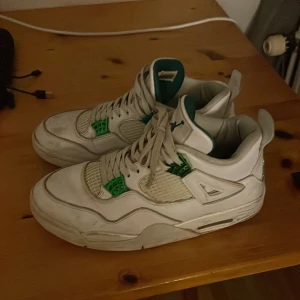 Jordan 4 green metallic - Säljer ett par vita Nike Air Jordans med gröna detaljer. Skorna har snörning och är i bra skick, perfekta för både vardag och sport. De har en klassisk design med hög komfort och stil. Passar perfekt för dig som vill ha en snygg och bekväm sneaker.