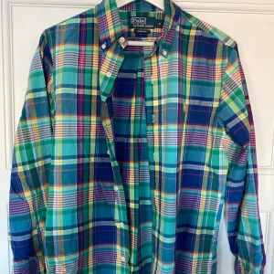 Rutig skjorta från Polo Ralph Lauren - Säljer en färgglad rutig skjorta från Polo Ralph Lauren i storlek S. Skjortan har en slim fit passform och är perfekt för både vardag och fest. Den har långa ärmar och knappar framtill. Färgerna är en mix av blå, grön, gul och röd. Superfräsch och stilren! 🌟