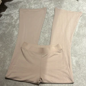 Beige yogapants från Gina Tricot - Beige yogapants mjukisbyxor från Gina Tricot i storlek XS. De är i ett mjukt och stretchigt material, perfekt för en avslappnad look. Mid waist och utsvängda längst ner. Perfekta för både vardag och mysiga hemmakvällar!