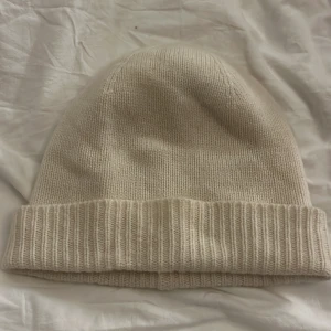 Vit kashmirmössa från Uniqlo - Säljer en supermjuk och stilren vit kashmirmössa från Uniqlo. Perfekt för att hålla dig varm under kalla dagar. Mössan har en ribbad kant som ger en snygg och bekväm passform. Passar till alla vinteroutfits! Inga fläckar eller defekter, knappt använd!