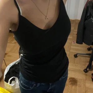 Svart linnetopp - Snygg och enkel svart linnetopp med smala axelband. Perfekt för sommardagar eller som lager under en jacka. Toppen har en tight passform och är gjord i ett mjukt och bekvämt material.