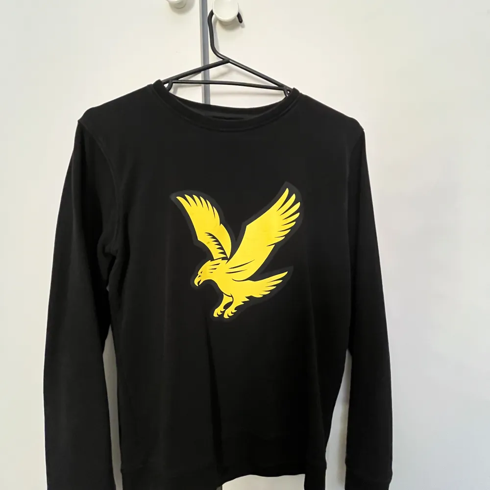 Säljer en svart långärmad tröja från Lyle & Scott med en cool gul örn på bröstet. Perfekt för höst och vår, och den är i mycket bra skick. Passar både till vardags och lite mer avslappnade tillfällen. Skön och stilren design!. Tröjor & Koftor.