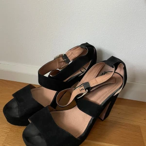 Svarta klackskor med remmar - Snygga svarta klackskor i mocka med breda remmar och öppen tå. Perfekta för festliga tillfällen! De har en stabil klack och justerbara spännen för bästa passform.