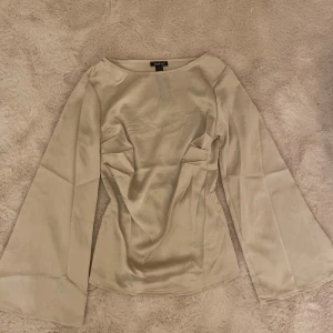 Satin/Silkes blus från Boohoo - Jätte fin beige blus från. Den är i silke/satin material och är beige. Den sitter inge bra på mig💕 Armarna går ut i slutet. Det går in i midjan (syns på bilderna). Helt oanvänd med prislappen kvar. Skriv för fler bilder eller frågor❤️
