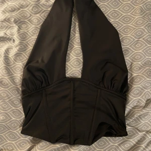 Svart topp med knytning  - Snygg svart topp med knytning i bra skick. Den har en stilren design med breda axelband och en djup rygg. Perfekt för fest eller sommardagar. Materialet känns mjukt och bekvämt mot huden. 🖤 (PM OM DU VILL HA FLER BILDER)