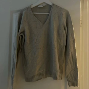 Beige stickad tröja från Vila - Mysig beige stickad tröja från Vila i mycket bra skick. Den har en v-ringad hals och långa ärmar, perfekt för kyliga höst- och vinterdagar. Ribbstickade muddar vid ärmslut och nederkant ger en snygg finish. Perfekt att matcha med jeans eller kjol för en avslappnad look.