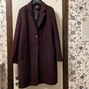 Vinröd kappa från Park Lane - Säljer en elegant vinröd kappa från Park Lane i mycket bra skick. Den har en klassisk design med två knappar framtill och långa ärmar. Perfekt för höst och vinter, och ger en stilren look. Kappan är gjord i ett ullmaterial som håller dig varm och bekväm. Endast använd ett fåtal ggr. Nypr.2.400kr