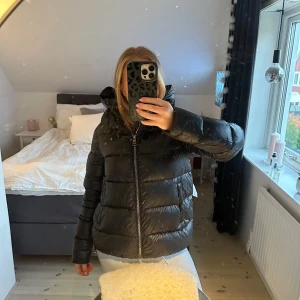 Svart dunjacka från Colmar - Säljer en snygg och varm svart dunjacka från Colmar. Jackan har en pufferstil med en hög krage och dragkedja framtill. Perfekt för kalla vinterdagar! Den är i bra skick och har en normal passform. Supermysig och stilren för både vardag och utgång 