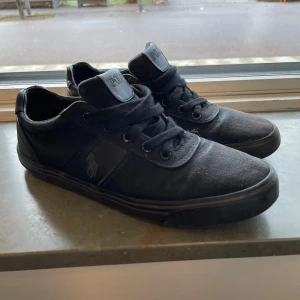 Svarta sneakers från Polo - Säljer ett par svarta sneakers från Polo. De är i bra skick och har en stilren design med snörning. Perfekta för vardagsbruk och passar till det mesta. Skorna har en diskret logga på sidan och är gjorda i ett slitstarkt material.