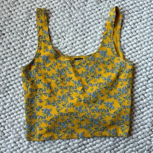 Gul blommig linnetopp från Gina Tricot - Säljer en superfin gul linnetopp från Gina Tricot med ett sött blått blommönster. Toppen är perfekt för sommaren med sin ärmlösa design och mjuka bomullsmaterial. Den har en normal passform och är i nyskick. Perfekt för en solig dag eller en avslappnad utflykt! 🌼💙