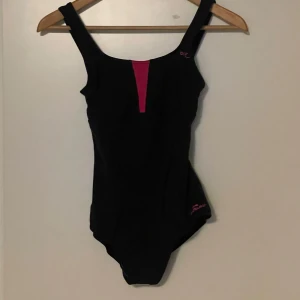 Svart baddräkt med rosa detaljer - Säljer en snygg och sportig svart baddräkt. Sparsamt använt.