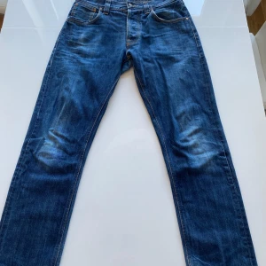 Blå jeans från Nudie Jeans Co - Säljer ett par klassiska blå jeans från Nudie Jeans Co i storlek W30 L32. De har en snygg, sliten look med orange sömmar. Dessa är uppsydda någon cm i benen därav de låga priset. Perfekta till skolan eller på stan! Tveka inte på att kontakta mig om frågor skulle uppstå!