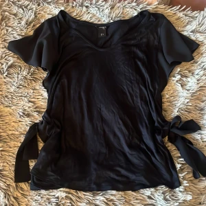 T-shirt med volanger och rosetter  - Mörk blå t-shirt med volanger på axlarna och knuta rosetter på sidan 