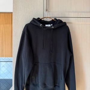 Svart hoodie från Weekday - Säljer en svart hoodie från Weekday i storlek S. Den är superbekväm och perfekt för både chill och vardagsbruk. Hoodien har en klassisk design med en stor ficka fram och justerbar huva med snören. Perfekt för höst och vinter!