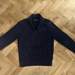 Mörk blå tröja från Polo Ralph Lauren - Säljer en stilren mörkblå tröja från Polo Ralph Lauren i storlek M. Tröjan har en dragkedja vid halsen och är perfekt för både vardag och lite finare tillfällen. Den är långärmad och gjord i ett mjukt material som känns skönt mot huden. Passar perfekt till höst och vinter! Ny pris 250€ mitt pris 740.